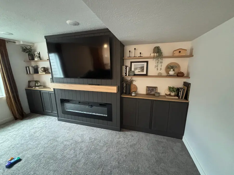 Finished basement family room with a dark media wall, built-in cabinets, open shelves, and carpet
