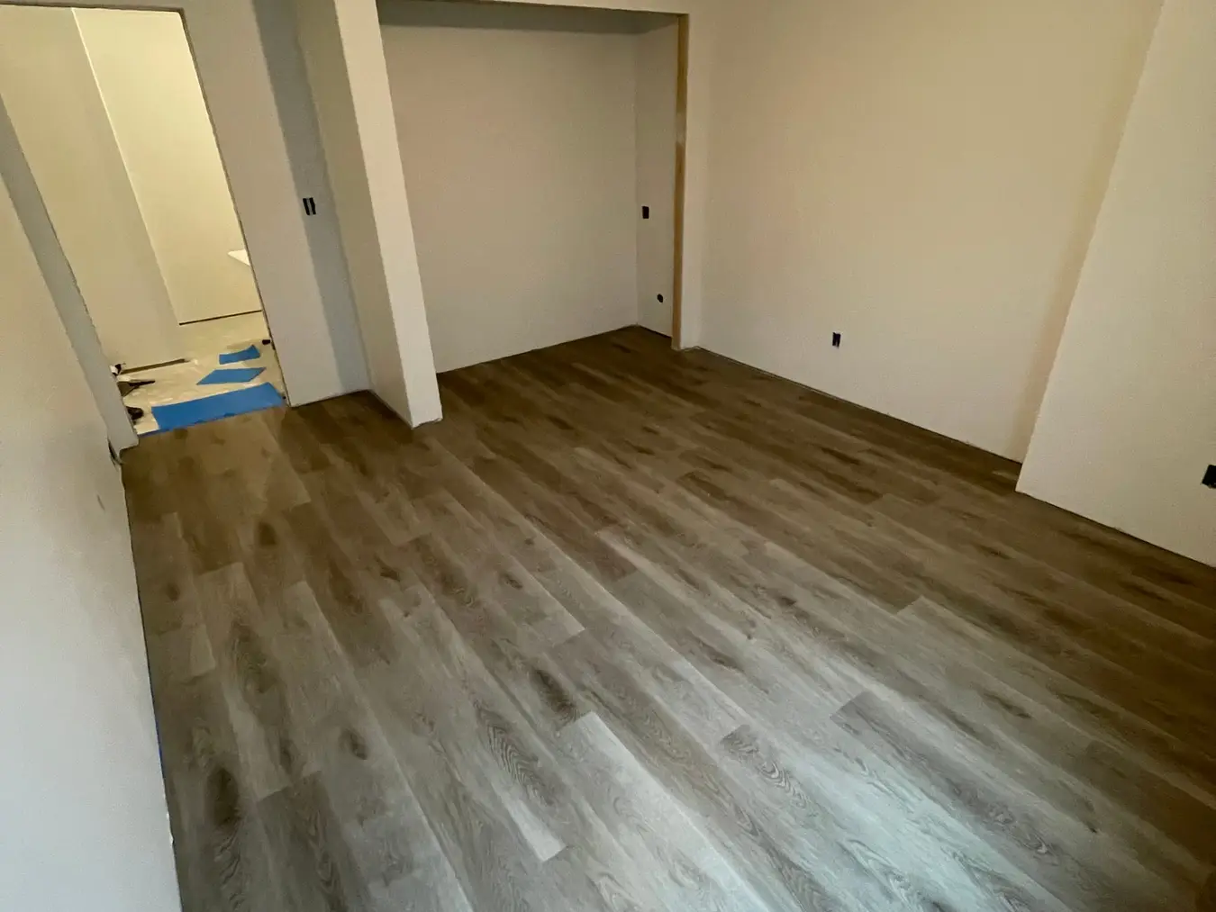 Basement bedroom in progress with new wood-look plank flooring and freshly painted walls