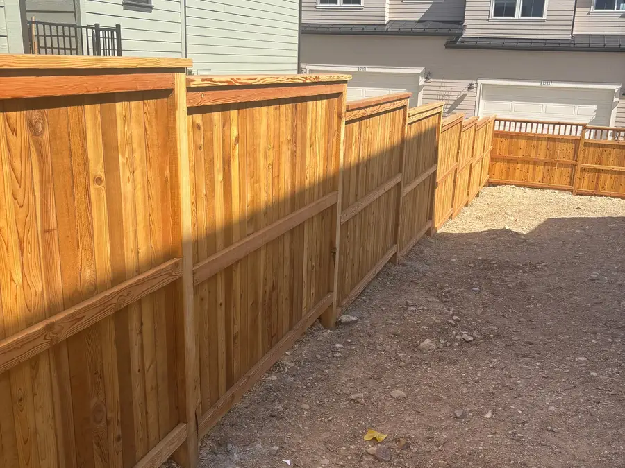 Cedar privacy fence with a top rail running along a new home