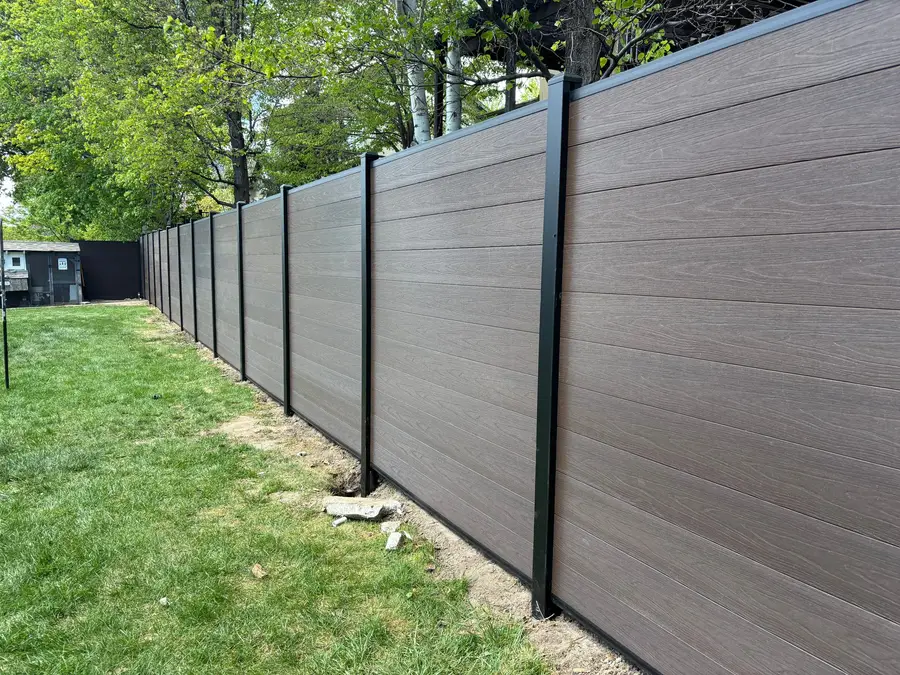Composite privacy fence with black posts along a lawn
