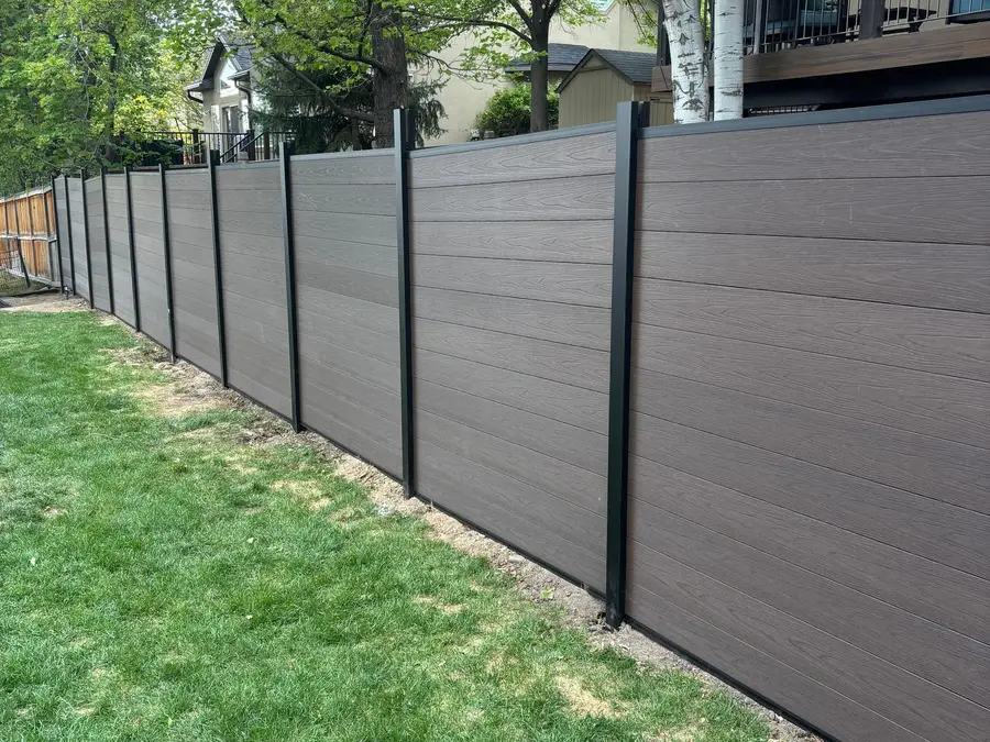Composite privacy fence along a green lawn with trees