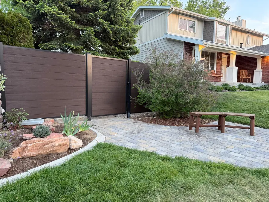 Composite privacy fence beside a paver path and bench in a front yard