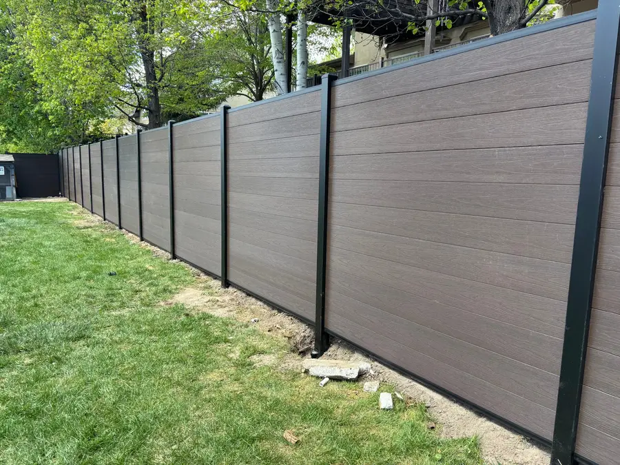 Horizontal composite privacy fence with black posts along a green lawn