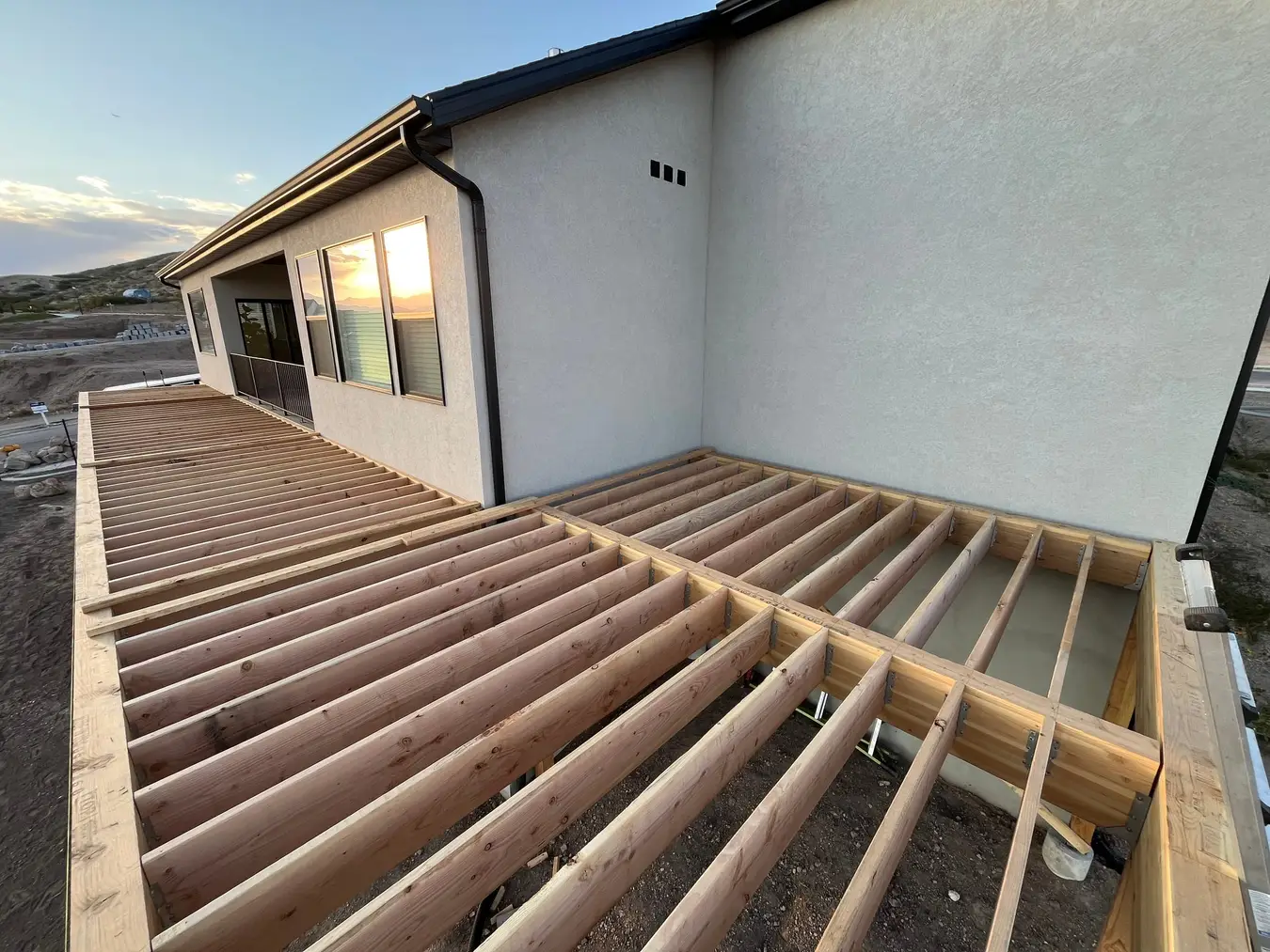 New deck framing with fresh joists wrapping around a home at sunset