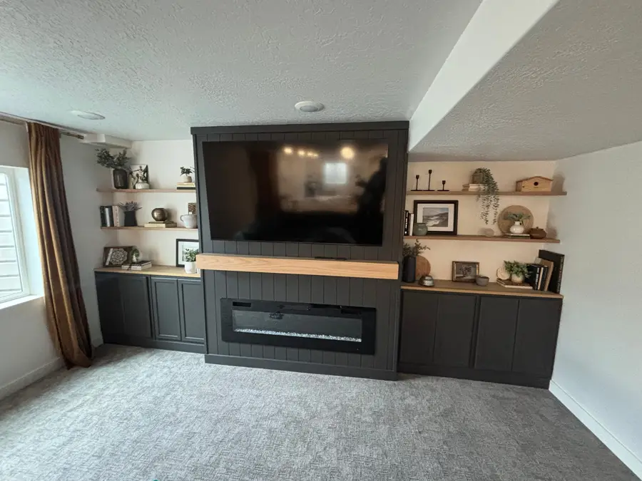Linear electric fireplace set into a dark shiplap wall with a wood mantel and built-ins