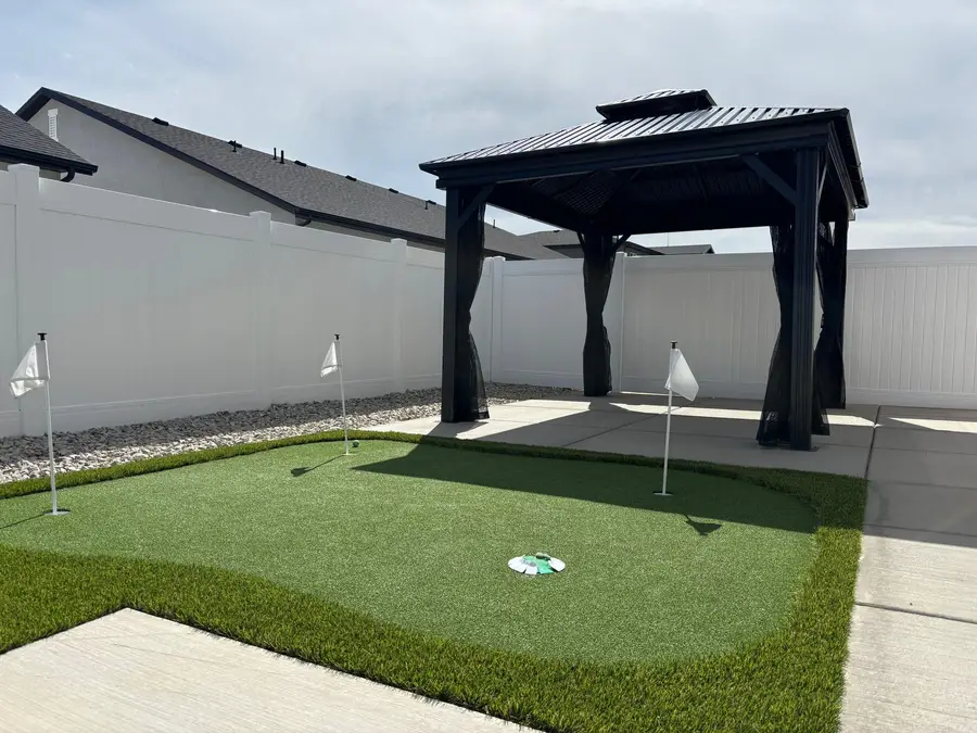 Black steel gazebo on a concrete pad next to a backyard putting green