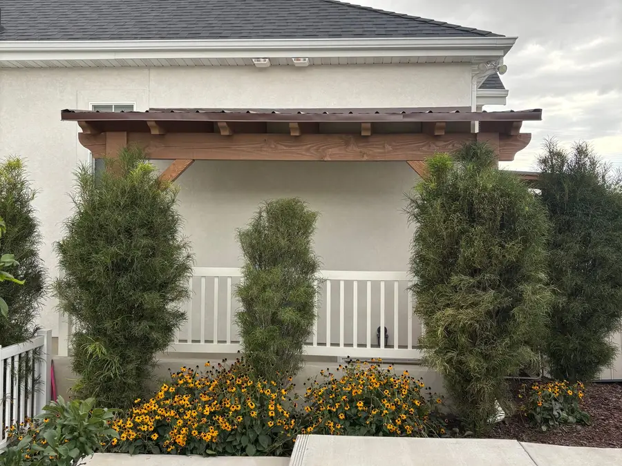 Front entry of a home with a cedar pergola, tall cypress trees, and flower beds