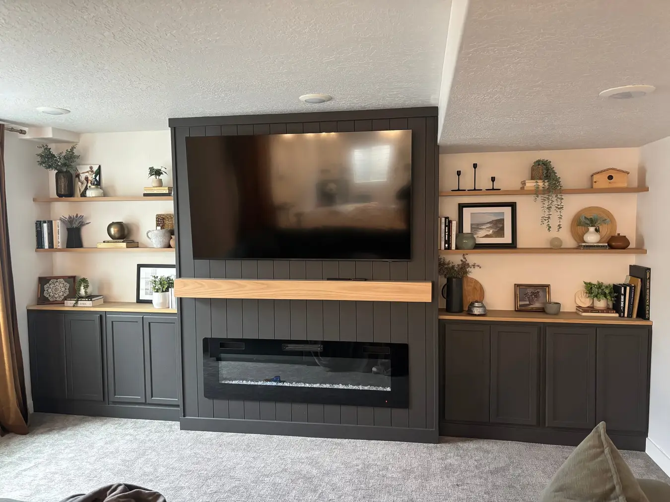 Dark green media wall with a linear electric fireplace, wood mantel, open shelves, and built-in cabinets