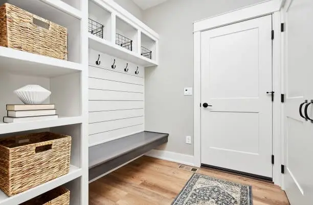 Mudroom with white built-in cubbies, a shiplap wall with coat hooks, a bench, and woven baskets