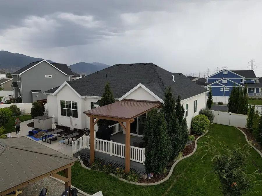 Covered patio with a pergola behind a home, seen from above with mountains in the distance