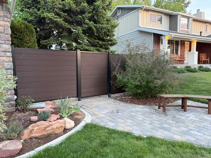 Paver patio with boulders, new plantings, a bench, and a composite privacy fence