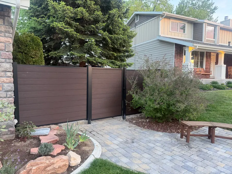 Paver patio with a wood bench, boulders, and new plantings beside a composite privacy fence