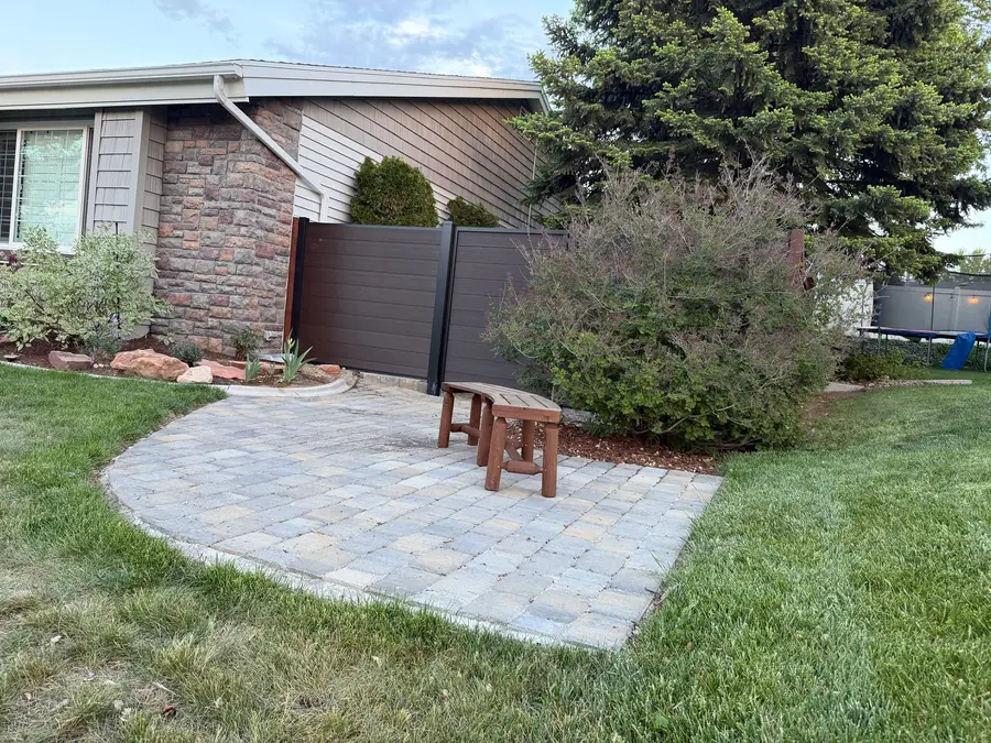 Paver patio corner with a wood bench beside the house and a composite fence