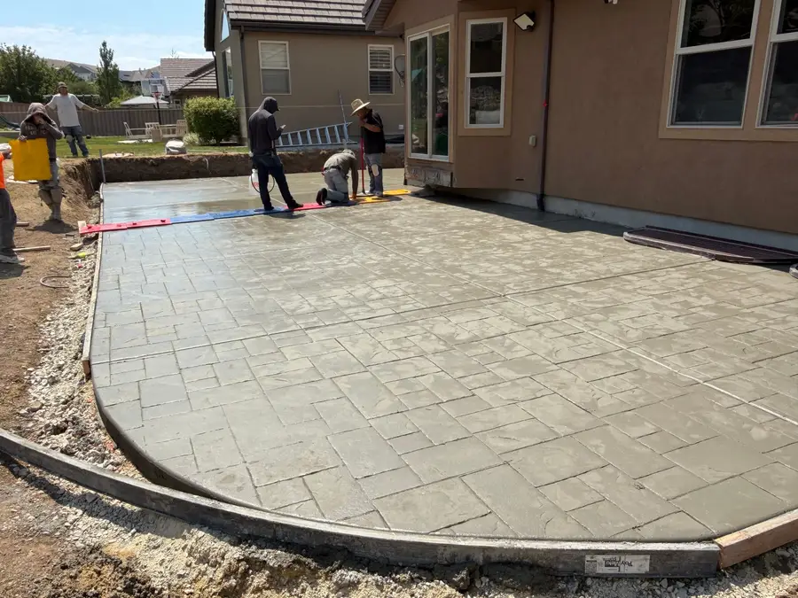 Crew finishing a freshly poured stamped concrete patio behind a home